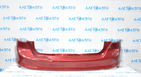 The rear bumper of a Ford Focus mk3 11-14 pre-restoration 5d red is dented, has tears, and has broken fasteners.