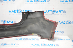 The rear bumper of a Ford Focus mk3 11-14 pre-restoration 5d red is dented, has tears, and has broken fasteners.