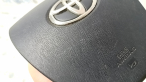The driver's side airbag in the steering wheel of a Toyota Prius V 12-17 is black and scratched.