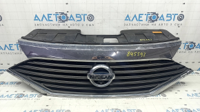 The grille assembly with the Nissan Quest 12-14 badge, camera, and molding is broken, worn, missing a fragment, broken fasteners, and peeling chrome.