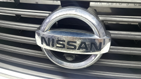 The grille assembly with the Nissan Quest 12-14 badge, camera, and molding is broken, worn, missing a fragment, broken fasteners, and peeling chrome.