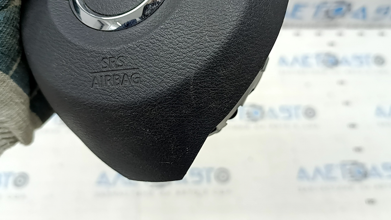 The driver's side steering wheel airbag for a Nissan Rogue 17-20 is black, has scratches, and is rusty.