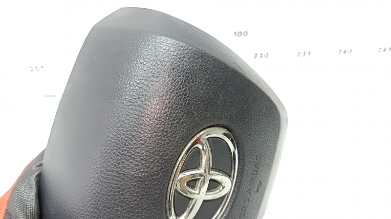 The Toyota Highlander 20-22 driver's steering wheel airbag is black and scratched.