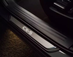 A set of black door sill plates for the Mazda CX-5 17-25 with a chrome insert and backlight, scratches